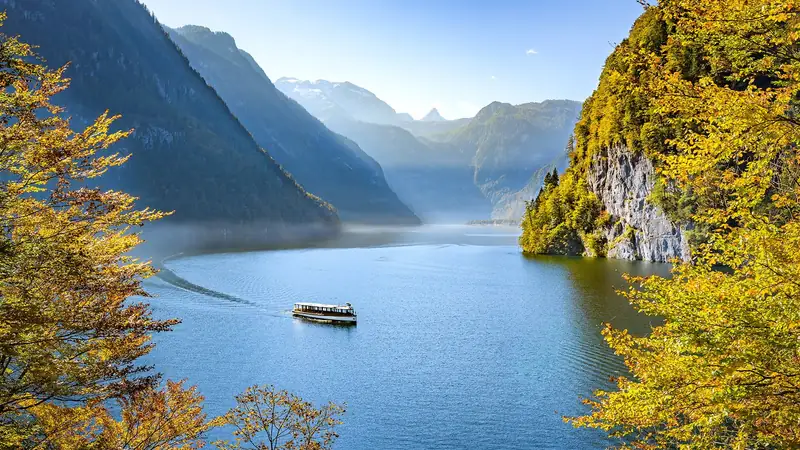 A passenger boat on Königssee between rock faces and autumn trees